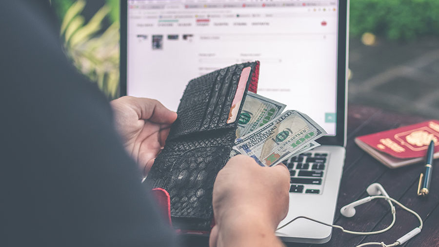 person holding money in front of laptop screen